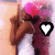 A person with long brown hair and a white top holds a pink heart-shaped object, with two white heart icons appearing in the center of the frame.