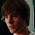 Pixelated close-up of a person with brown hair and light skin, cropped to show the head and upper shoulders against a dark background.