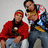 Two pixelated figures in red and multicolored tops pose against a light gray background with visible digital compression artifacts.