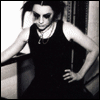 Black-and-white image of a person in a sleeveless dress with hands on hips, standing against a patterned background.