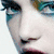 A close-up of a person's face with blue eyeshadow, pink lips, and a neutral expression, cropped to show eyes, nose, and mouth.