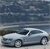 A silver sedan with a black roof is positioned on a road under a cloudy sky, viewed from a low angle.