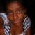 Pixelated image of a person with brown skin tone holding a silver and black checkered object near their face against a dark background.