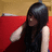 A pixelated image of a person with long dark hair wearing a sleeveless top, seated against a red and beige background.