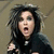 A pixelated image of a person with dark hair and open mouth, wearing black clothing against a muted background.