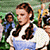 A pixelated image shows a person with long brown hair wearing a white and blue outfit, standing in front of a green background with other figures partially visible.