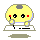 Pixelated yellow circular character with gray top spot, black eyes, red cheeks, and blue outline holding a white object over a keyboard-like base.