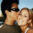 Two people in close physical proximity, one with dark hair and sunglasses, the other with light brown hair; a red stylized anchor symbol on white background.