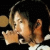repeated images showing a person with short dark hair wearing a black top with white collar, holding a microphone near their mouth, with yellow text overlays changing across frames