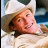 A static image of a person wearing a light-colored cowboy hat and brown jacket, with text overlay reading "He ain't no queer!" in black serif font.