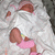 A baby in a white blanket with pink accents lies on its back, legs bent and feet visible.