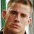 Pixelated close-up of a person's face with light brown hair, visible ear, and partial green and white background elements.