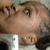A pixelated image of a person with light skin and dark hair lying down, wearing a white shirt, with a purple figure standing nearby.