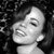 Black-and-white pixelated image of a person with closed eyes and a broad smile, dark hair, and a light-colored garment against a dark background.