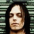 A person with long dark hair and pale skin appears in three against a striped background, with the bottom cropped to show only the upper body