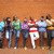Group of people standing in a line against an orange background with one person holding a red and white striped sign.