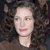 Pixelated close-up of a person with dark curly hair against a dark background, wearing a light-colored top.