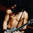 Pixelated image of a shirtless person with light brown skin lying on their back against dark background, arms raised above head.
