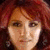 A pixelated close-up of a person with reddish-brown hair wearing a pink patterned top, with a blurred background.