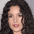 Pixelated close-up of a person with dark curly hair, light skin, and pink lips against a gray background.