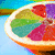 A sliced citrus fruit with multicolored segments in red, purple, green, and blue on a light blue background.