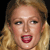 Pixelated close-up of a person with light brown hair, blue eyes, and red lips, mouth open in a shout or yell against a black background.