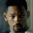 Pixelated close-up of a person's face with dark hair, light skin, and a neutral expression against a muted blue-gray background.