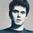 A pixelated image of a person with dark hair and light skin wearing a dark shirt against a plain background.