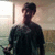 Pixelated image of a person in profile wearing a dark cap and dark shirt, standing against a light-toned background with vertical and horizontal elements.