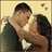 A pixelated static image shows two figures embracing, one with short dark hair wearing a white shirt and the other with long dark hair in a black top against a light beige background.