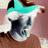 Pixelated static image of a character with teal hair, white face, dark clothing, and brown background elements.