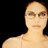 Pixelated static image of a person with light skin tone wearing glasses and a thin-strapped top against black background, cropped to show upper body from shoulders up.