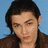 Pixelated image of a person with dark hair and brown clothing against light blue background, paired with cyan text on black