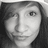 Grayscale pixelated portrait of a person with long dark hair, neutral expression, and visible eye and nose details.