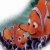 Two orange clownfish with white stripes swim in a pixelated underwater scene, one larger fish positioned behind and to the right of a smaller fish.