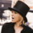 Pixelated image of a person wearing a black wide-brimmed hat and dark clothing, with light-colored hair visible beneath the brim.