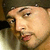 A pixelated image of a person with light skin and dark hair wearing a cap, positioned next to another figure in blue clothing against a red-and-white background.