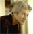 Pixelated static image of a person with light-colored hair wearing a dark top against a light background with vertical stripes.