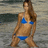 Pixelated image of a person in blue bikini standing on beach with water and sand background.