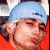 A person wearing a light blue headband with dark text, orange clothing, and white hair appears in two side-by-side showing slight facial expression changes