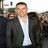 Pixelated static image of a person in dark jacket and white shirt with blurred background elements.