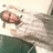 Pixelated image of a person with light skin and brown hair lying on their back, wearing white top and dark green pants against a pale background.