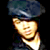 Pixelated static image of a person wearing a dark blue cap and light-colored shirt against black background, with bright lighting on face.