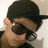 A person wearing a black cap and dark sunglasses appears in four -aligned with slight variations in head position and background brightness