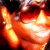 A person with dark hair and sunglasses smiles broadly, showing teeth in a warm expression.