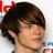 Pixelated close-up of a person's head and shoulders with dark hair, visible ear, and partial neck against a light background with red elements.