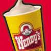 Yellow Wendy's cup with soft-serve ice cream, red background, and partial text fragments reading 'it's the only soquid...' and '...you eat with a spoon.'