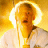 Pixelated static image of a person with light hair wearing white clothing against a bright yellow background, featuring a glowing halo effect around the head.