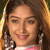 Pixelated close-up of a smiling person with long brown hair wearing earrings and a pink-and-white top against a blurred background.