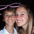 Two people in white shirts pose closely together under a purple bow graphic, with one person's head slightly turned toward the other.